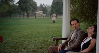 Movie still from “Broadcast News” (1987), directed by James L. Brooks – A man sitting on top of a wooden bench in a park; Medium shot, Over the shoulder angle