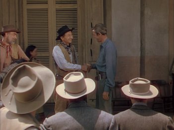 Movie still from “Broken Arrow” (1950), directed by Delmer Daves – Two men shaking hands in front of a group of people wearing cowboy hats; Medium shot, Over the shoulder angle