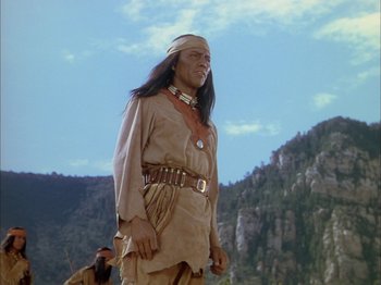 Movie still from “Broken Arrow” (1950), directed by Delmer Daves – A man dressed as a native american standing in front of a mountain range; Medium shot, Low angle