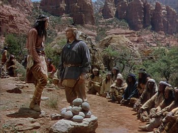 Movie still from “Broken Arrow” (1950), directed by Delmer Daves – A group of people sitting on top of a dirt road; Wide shot, Over the shoulder angle