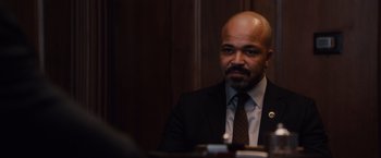 Movie still from “Broken City” (2013), directed by Allen Hughes – A man in a suit sitting at a table in a room; Close Up shot, Over the shoulder angle