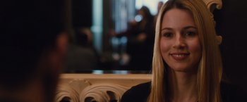 Movie still from “Broken City” (2013), directed by Allen Hughes – A woman sitting in a chair smiling for the camera; Close Up shot, Over the shoulder angle