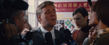 Movie still from “Broken City” (2013), directed by Allen Hughes – A man in a suit and tie talking into microphones in front of other people; Close Up shot, Over the shoulder angle