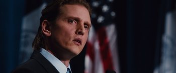 Movie still from “Broken City” (2013), directed by Allen Hughes – A person speaking on a microphone in front of an american flag; Close Up shot, Low angle
