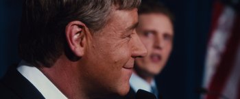 Movie still from “Broken City” (2013), directed by Allen Hughes – A man is talking into a microphone while another man looks on; Close Up shot, Over the shoulder angle