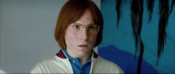 Movie still from “Broken Embraces” (2009), directed by Pedro Almodóvar – A man with long red hair wearing glasses and a white jacket; Close Up shot, Low angle