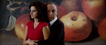 Movie still from “Broken Embraces” (2009), directed by Pedro Almodóvar – A man and a woman standing next to each other in front of a painting; Medium shot, Low angle