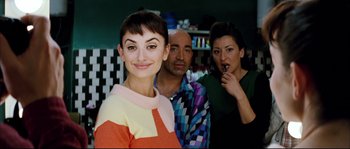 Movie still from “Broken Embraces” (2009), directed by Pedro Almodóvar – A woman posing for a picture with two men; Medium shot, Over the shoulder angle