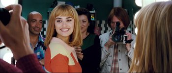 Movie still from “Broken Embraces” (2009), directed by Pedro Almodóvar – A woman smiles while a man takes a picture of her; Close Up shot, Over the shoulder angle