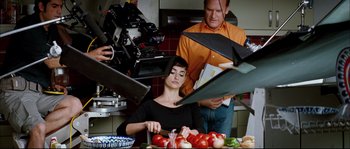Movie still from “Broken Embraces” (2009), directed by Pedro Almodóvar – A woman sitting in front of a table of food; Medium shot, Over the shoulder angle
