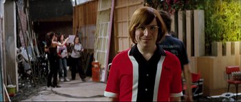 Movie still from “Broken Embraces” (2009), directed by Pedro Almodóvar – A man in a red and black shirt is standing outside; Medium shot, Over the shoulder angle