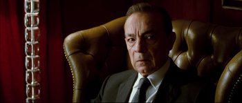 Movie still from “Broken Embraces” (2009), directed by Pedro Almodóvar – An older man wearing a suit and tie sitting in a chair; Close Up shot, Low angle