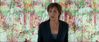 Movie still from “Broken Embraces” (2009), directed by Pedro Almodóvar – A woman standing in front of a painting of flowers; Medium shot, High angle