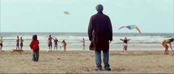 Movie still from “Broken Embraces” (2009), directed by Pedro Almodóvar – A man standing on the beach looking at people flying kites in the water; Wide shot, Over the shoulder angle