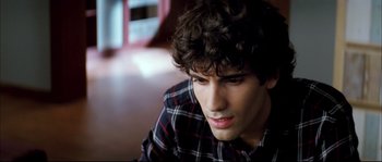 Movie still from “Broken Embraces” (2009), directed by Pedro Almodóvar – A young man sitting on the ground looking at the camera; Close Up shot, High angle