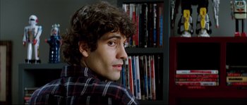 Movie still from “Broken Embraces” (2009), directed by Pedro Almodóvar – A man sitting in front of a book shelf; Close Up shot, Over the shoulder angle