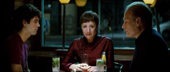 Movie still from “Broken Embraces” (2009), directed by Pedro Almodóvar – A woman sitting at a table with a drink in front of her; Medium shot, Over the shoulder angle