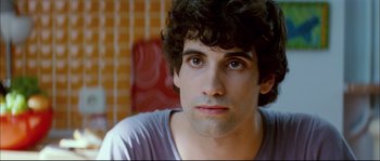 Movie still from “Broken Embraces” (2009), directed by Pedro Almodóvar – A person with curly black hair; Close Up shot, Over the shoulder angle