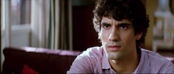Movie still from “Broken Embraces” (2009), directed by Pedro Almodóvar – A man sitting on a couch looking at the camera; Close Up shot, Over the shoulder angle