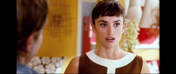 Movie still from “Broken Embraces” (2009), directed by Pedro Almodóvar – A person wearing a brown and white dress; Close Up shot, Over the shoulder angle
