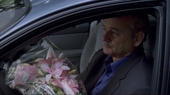 Movie still from “Broken Flowers” (2005), directed by Jim Jarmusch – A man sitting in the back of a car holding a bouquet of flowers; Close Up shot, Over the shoulder angle