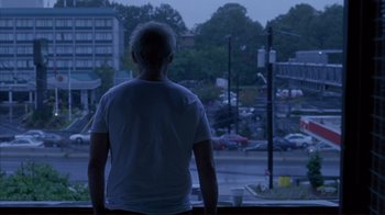 Movie still from “Broken Flowers” (2005), directed by Jim Jarmusch – A man standing in front of a window looking out at a city; Wide shot, Low angle