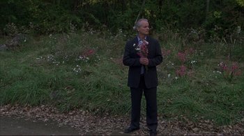 Movie still from “Broken Flowers” (2005), directed by Jim Jarmusch – A man in a suit holding a bouquet of flowers; Wide shot, Over the shoulder angle