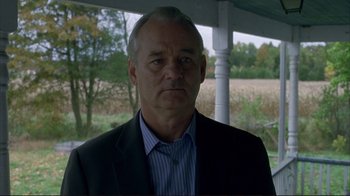 Movie still from “Broken Flowers” (2005), directed by Jim Jarmusch – A man wearing a suit and striped shirt is standing in front of trees; Close Up shot, Over the shoulder angle