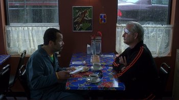 Movie still from “Broken Flowers” (2005), directed by Jim Jarmusch – Two men sitting at a table in front of a cup of coffee; Medium shot, Over the shoulder angle