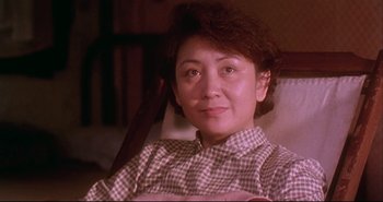 Movie still from “Bullet in the Head” (1990), directed by John Woo – A woman sitting in a chair in a plaid shirt; Close Up shot, Low angle