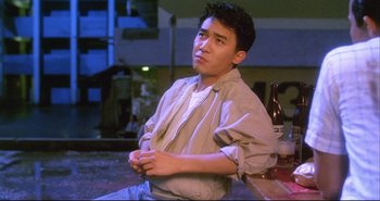Movie still from “Bullet in the Head” (1990), directed by John Woo – A man sitting at a table with a bottle of beer; Medium shot, Low angle