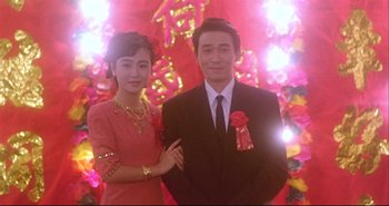 Movie still from “Bullet in the Head” (1990), directed by John Woo – A man and a woman standing next to each other in front of lights; Medium shot, Low angle