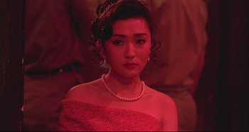 Movie still from “Bullet in the Head” (1990), directed by John Woo – A woman in a red dress and a pearl necklace; Close Up shot, Over the shoulder angle