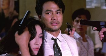 Movie still from “Bullet in the Head” (1990), directed by John Woo – A man and a woman are surrounded by a group of people; Close Up shot, Over the shoulder angle