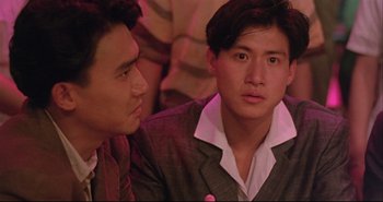 Movie still from “Bullet in the Head” (1990), directed by John Woo – Two young men sitting next to each other in front of a crowd of onlookers; Close Up shot, Over the shoulder angle