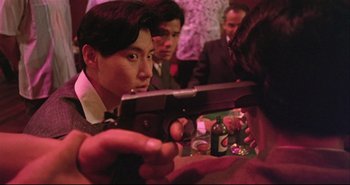 Movie still from “Bullet in the Head” (1990), directed by John Woo – A group of people sitting at a table holding guns; Close Up shot, Over the shoulder angle