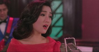 Movie still from “Bullet in the Head” (1990), directed by John Woo – A woman in a red dress singing into a microphone; Close Up shot, High angle