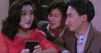 Movie still from “Bullet in the Head” (1990), directed by John Woo – A group of people sitting on a couch looking at a cell phone; Medium shot, High angle