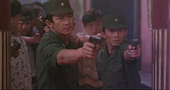 Movie still from “Bullet in the Head” (1990), directed by John Woo – A group of men in uniform holding a gun; Medium shot, Over the shoulder angle