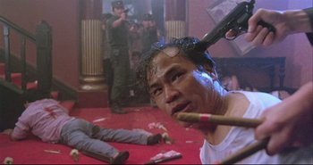 Movie still from “Bullet in the Head” (1990), directed by John Woo – A man is smoking a cigarette while another man is holding a gun; Medium shot, Low angle