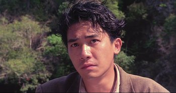 Movie still from “Bullet in the Head” (1990), directed by John Woo – A young man with black curly hair wearing a brown jacket; Close Up shot, High angle