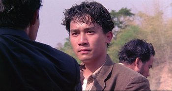 Movie still from “Bullet in the Head” (1990), directed by John Woo – A young man with curly black hair is looking at the camera; Close Up shot, Low angle