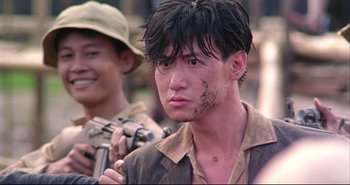 Movie still from “Bullet in the Head” (1990), directed by John Woo – A man in a hat is holding a gun and looking at the camera; Close Up shot, Over the shoulder angle