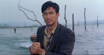 Movie still from “Bullet in the Head” (1990), directed by John Woo – A man in a suit and tie holding a small object; Medium shot, Low angle