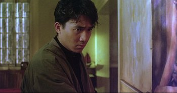 Movie still from “Bullet in the Head” (1990), directed by John Woo – A man in a brown jacket is standing in a room; Close Up shot, Low angle