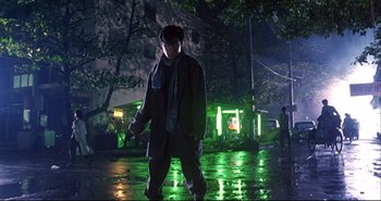 Movie still from “Bullet in the Head” (1990), directed by John Woo – A man standing in the rain at night holding a knife; Wide shot, Low angle