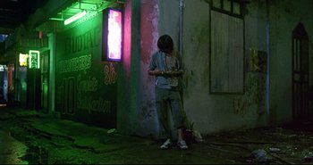 Movie still from “Bullet in the Head” (1990), directed by John Woo – A person standing on the sidewalk using a cell phone; Wide shot, High angle