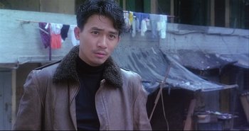 Movie still from “Bullet in the Head” (1990), directed by John Woo – A man wearing a leather jacket standing in front of a building; Close Up shot, Low angle