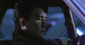 Movie still from “Bullet in the Head” (1990), directed by John Woo – A man sitting in the driver's seat of a car at night; Close Up shot, Low angle