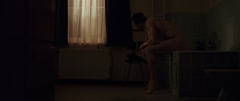 Movie still from “Bullhead” (2011), directed by Michaël R. Roskam – A naked man sitting on a chair in a dark room; Wide shot, High angle